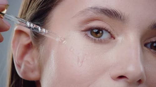 Woman Applies Serum to Face with Glass Dropper