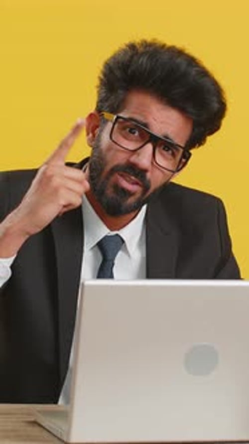 Serious Businessman Explaining with Hand Gestures Near Laptop
