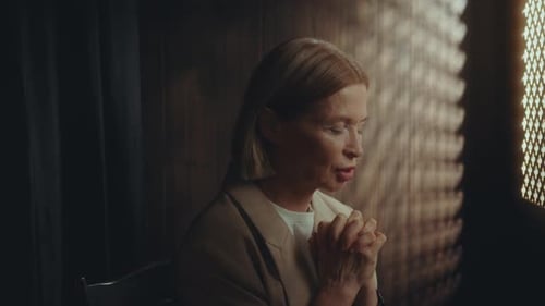 Elderly Woman Saying Prayer in Dimly Lit Confessional Booth