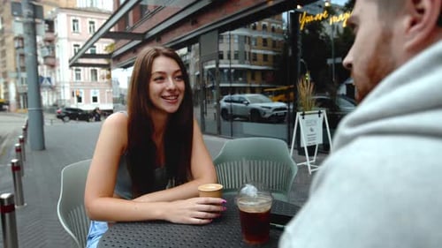Attractive young couple having lunch sitting at cafe table outdoors, drinking coffee and talking.