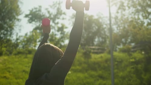 Woman Exercising with Dumbbells Outdoors in Sunlight
