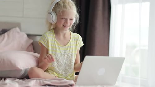 Blondes Schulmädchen, das zu Hause auf dem Bett studiert und Hausaufgaben mit Laptop-Fernunterricht online macht