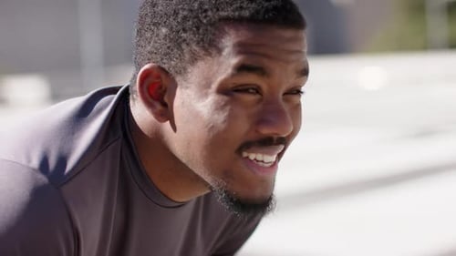 Finishing sprint, African American male athlete bending over breathing and resting on sunlit deck