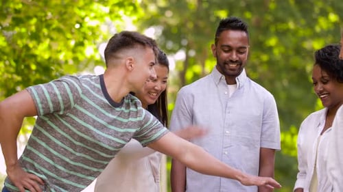 Smiling multiethnic friends stacking hands in summer park symbolizing global unity