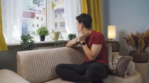 Man Sitting, Thinking, on Couch Indoors During Day
