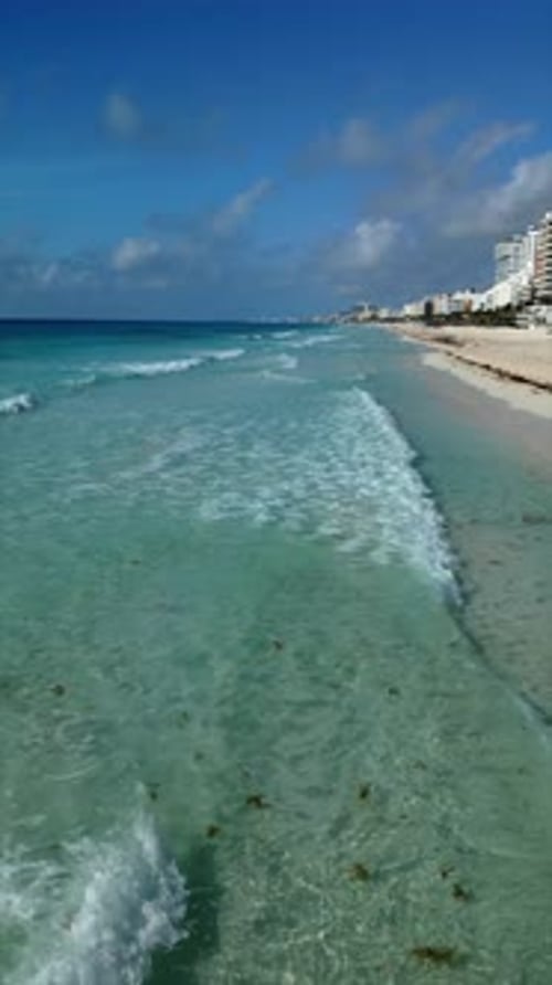 Drone flight on the shore of a tourist beach. Waves breaking on the shore with the calm tide.