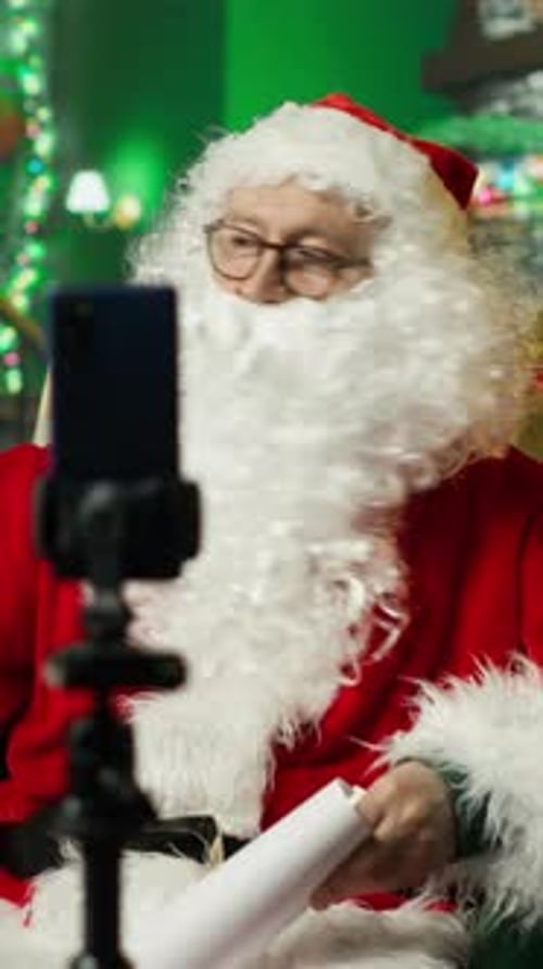 Vertical Video Santa Claus Filming with Phone on Tripod Reading Letters From Kids Showing Set