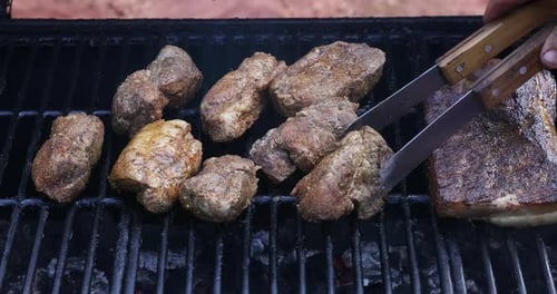 Tongs Moving Grilled Meat on a Grill