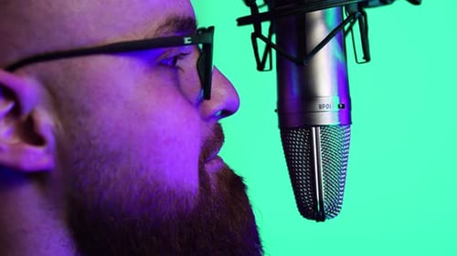 Man With Beard and Glasses Speaking in Front of Professional Microphone With Green Screen Background