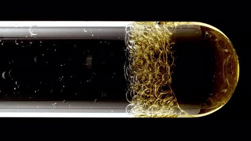 Foto macro de bolhas douradas de diferentes tamanhos descendo em tubo de ensaio de vidro sobre fundo preto