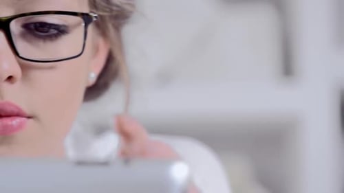 Focused young woman with glasses uses tablet