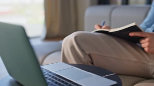 Man Writing in Notebook with Laptop at Home