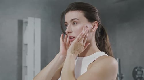 Woman Applies Cream To Face in Bathroom