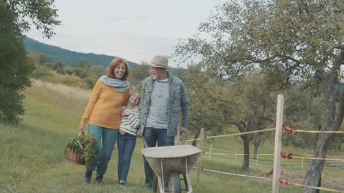 Grandparents and Grandchild Walking with Wheelbarrow on Farm