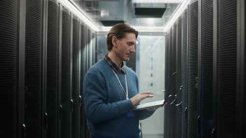 Portrait of Network Engineer Monitoring Servers with laptop in Data Center