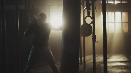 Man Punching Heavy Bag in Smoky Gym