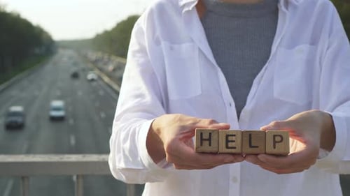 Porträt einer jungen, stilvollen, schönen Frau in Weiß, steht auf einer Brücke und hält Würfel mit dem Wort HELP