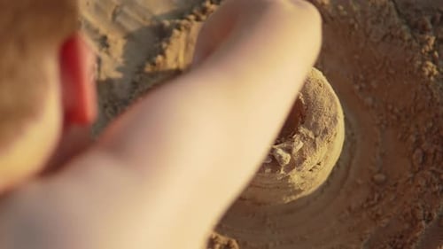 Child Builds Sand Castle Turret on Beach View Over the Shoulder