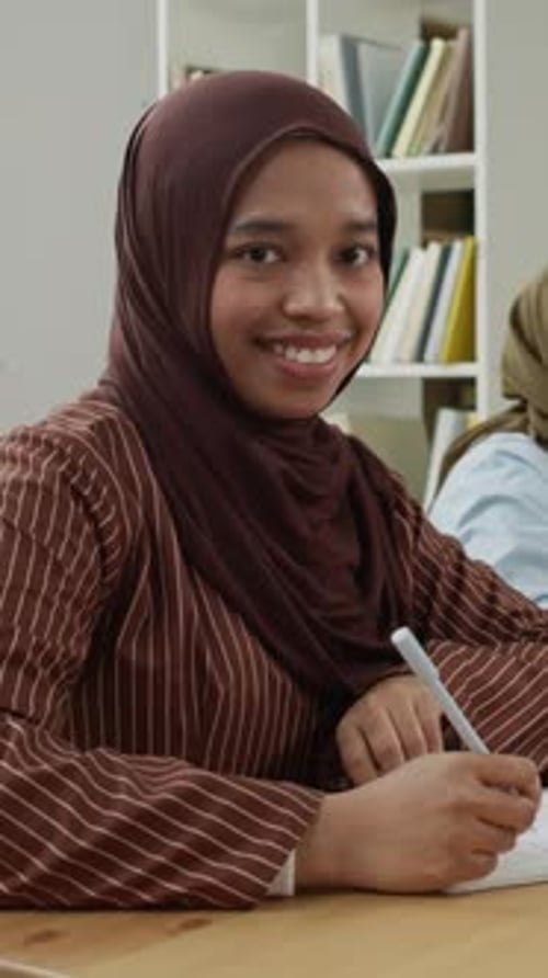 Porträt einer asiatischen muslimischen Studentin, die im Klassenzimmer lächelt und schreibt