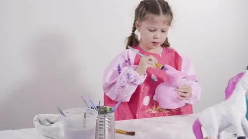 Kleines Mädchen malt Pappmaché-Figuren mit Acrylfarbe für ihr Homeschooling-Kunstprojekt
