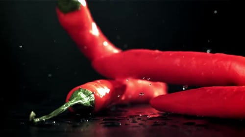 Chili Peppers fallen auf einen nassen schwarzen Tisch, gefilmt mit einer Hochgeschwindigkeitskamera mit 1000 Bildern pro Sekunde