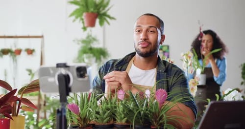 Hombre sonriente, bloguero de redes sociales, florista grabando un videotutorial de floristería, grabando un vlog en flor