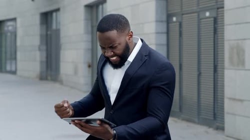 Worried african american businessman reads bad news on tablet screen in city street