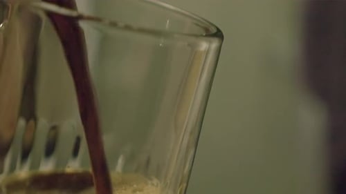 Frothy draft beer is poured into glass in close up view, bar interior