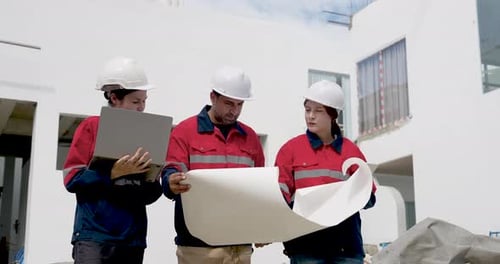 Asiatische Ingenieurin hält einen Bauplan in der Hand, während ein männlicher Manager die Zwischenablage liest und der Auftragnehmer das Team plant