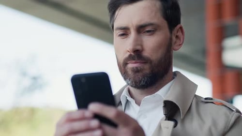 Close Up Face Serious Stylish Handsome Man with Beard in Coat Uses Smartphone Stand in Part at