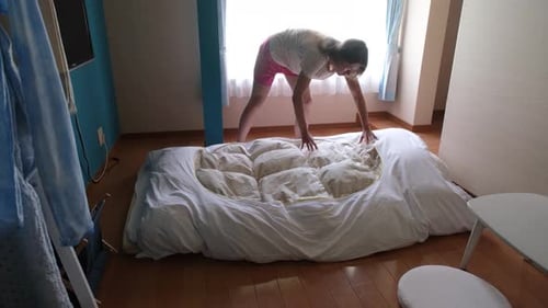 Young Adult Making Bed in Bright Room