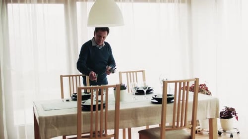 Man Setting Dining Table in Bright Home