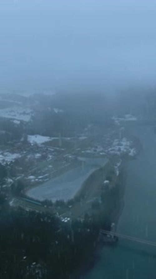 Winter Landscape Reveals Quiet Village in Misty Weather with a River Hills and Snowcovered Ground
