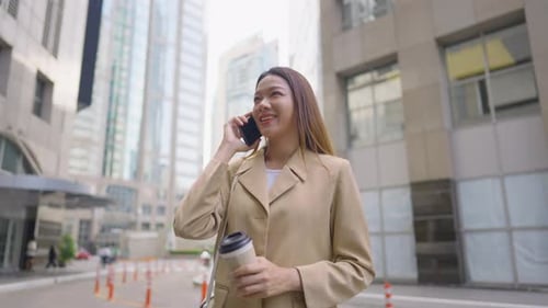 Asian young businesswoman talking on smartphone while standing in city.