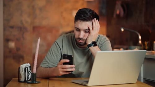 Young Adult Using Phone with Laptop on Table