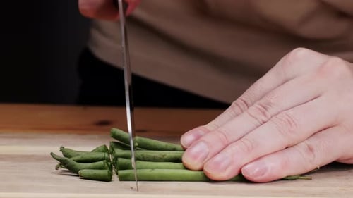 Frische grüne Bohnen mit dem Messer auf einem Holztisch schneiden, eine Grundnahrungszutat liegt auf einem Holztisch