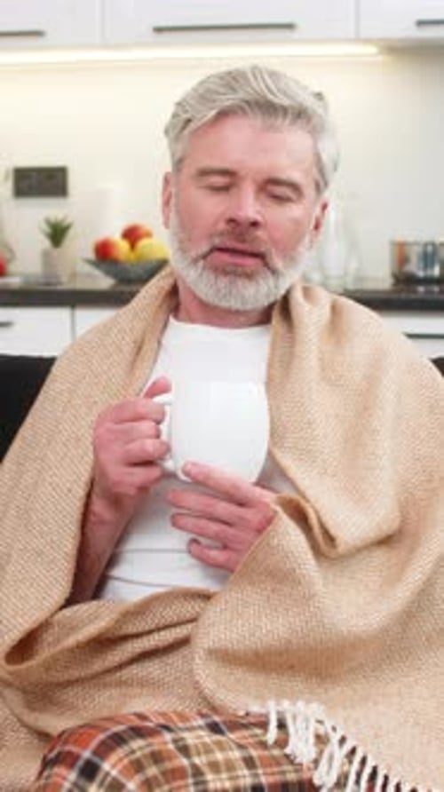 Man Wrapped in Blanket Drinking from a Mug