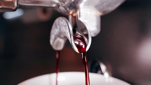 Close Up View of Dark Reddish Espresso Stream Flowing From Portafilter Spout Into Cup Showing