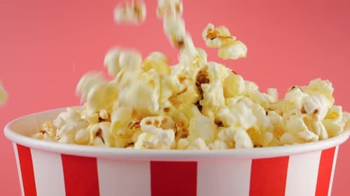 Popcornkörner fallen einzeln auf rot-weiß gestreiftem Hintergrund in einen rot-weiß gestreiften Eimer