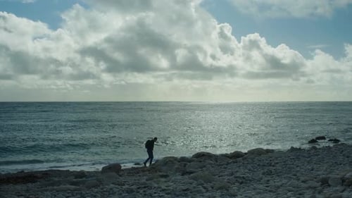 4K Slow motion panoramic landscape shot of a man walking on the rocky beach of Church Ope, on the is