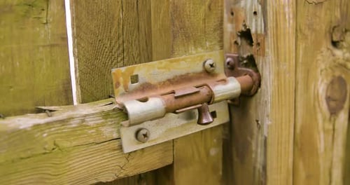 Man Unlatching Old Sliding Lock and Opening Gate