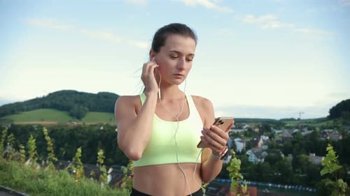 Woman Using Phone and Earbuds Outdoors
