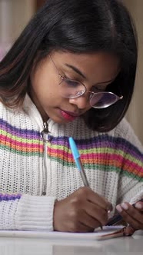 African Latin American Young Woman with Glasses Uses Calculator and Writes Notes at Home
