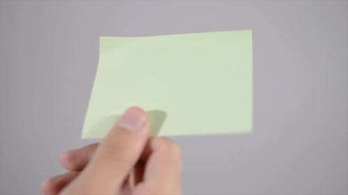 Hand Smooths Light Green Sticky Note onto Surface