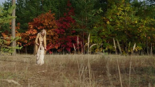 An Active Woman Plays with a Golden Retriever Puppy in the Autumn Forest Against the Background of