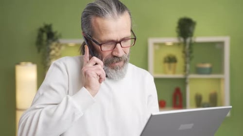 Adult Using Laptop and Talking on Phone at Home