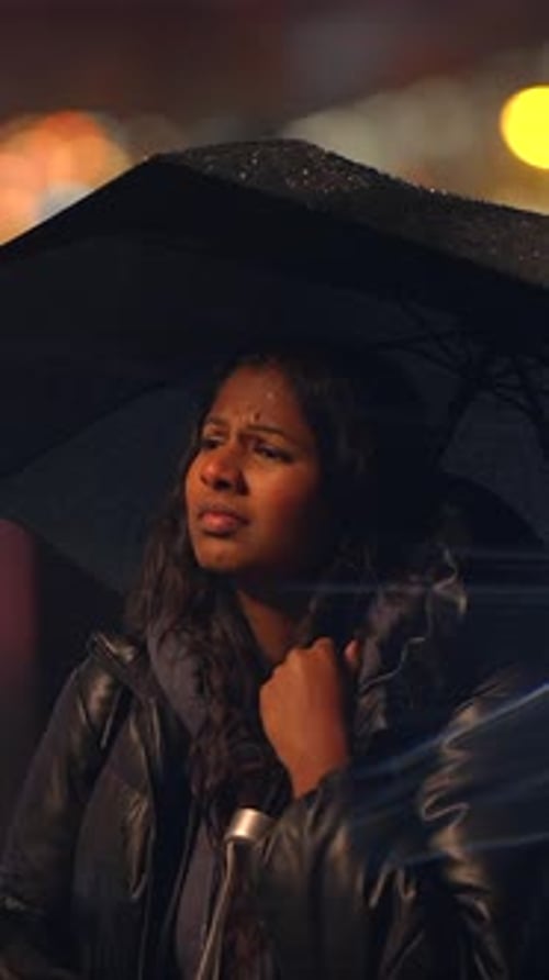 A Woman Holding an Umbrella Stands in a Rainy City During a Night Filled with Ambiance