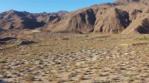 Low drone shot over floor of arid landscape approaching close barren mountains.