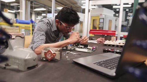 Focused southeast asian engineer examines circuit board in research lab