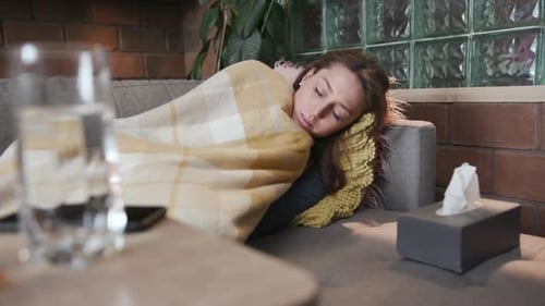 Sick Woman Resting on Couch Indoors Under Blanket